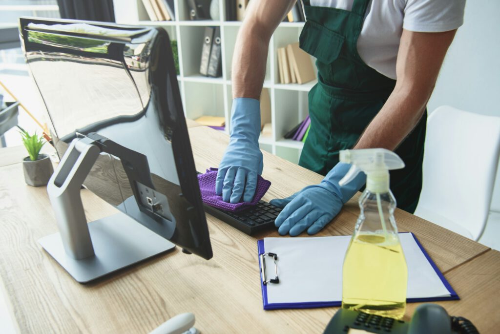 cropped shot of professional cleaner in rubber gloves cleaning computer keyboard in office